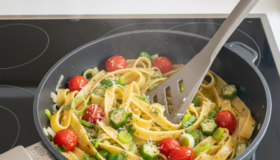 Frisch zubereitete Bandnudeln mit Okraschoten, leuchtend roten Kirschtomaten und knackigem Lauch, appetitlich angerichtet und dampfend heiß direkt aus der Pfanne serviert.