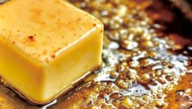 Braune geschmolzene nussige Butter in einer schwarzen Pfanne mit einem Stück frisch Butter.