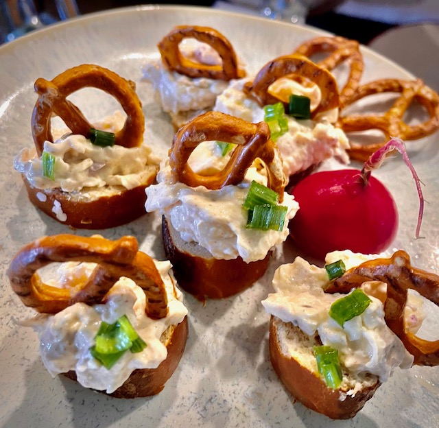 Einige Brezn Obatzter Häppchen auf einem weißen Teller mit einem Radieschen angerichtet als bayerisch Tapas passen auch hervorragend zu deiner bayirsch Hummus Variante.
