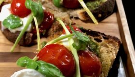 Bruschetta mit Burrata und Pesto mit Basilikum dekoriert und auf einem Tablett serviert.
