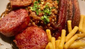 Cotechino mit Linsen, Speck, Salsiccia und Würstchena uf einem Teller serviert.