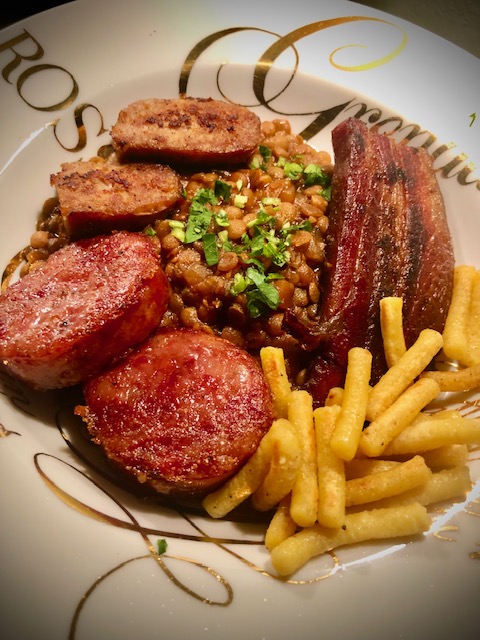 Cotechino mit Linsen, Speck, Salsiccia und Würstchena uf einem Teller serviert.
