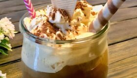 Eiskaffee veredelt mit Vanilleeis, Milch, Sirup und Sahne, dekorativ im Glas serviert.