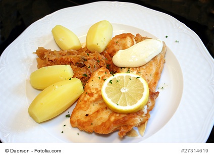 Fischfilet im Bierteigmantel mit Kartoffeln auf einem hellen Teller serviert.