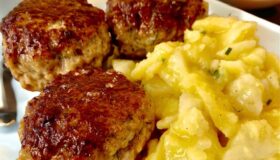 Fleischpflanzerl mit Kartoffelsalat auf einem weißen Teller serviert.
