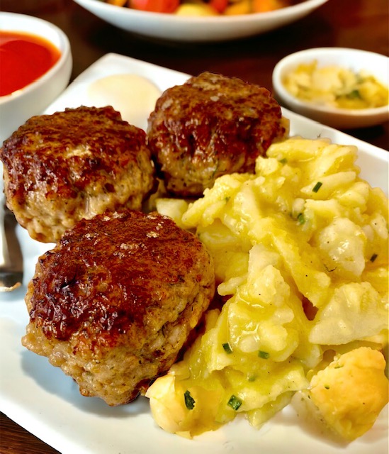 Fleischpflanzerl mit Kartoffelsalat auf einem weißen Teller serviert.
