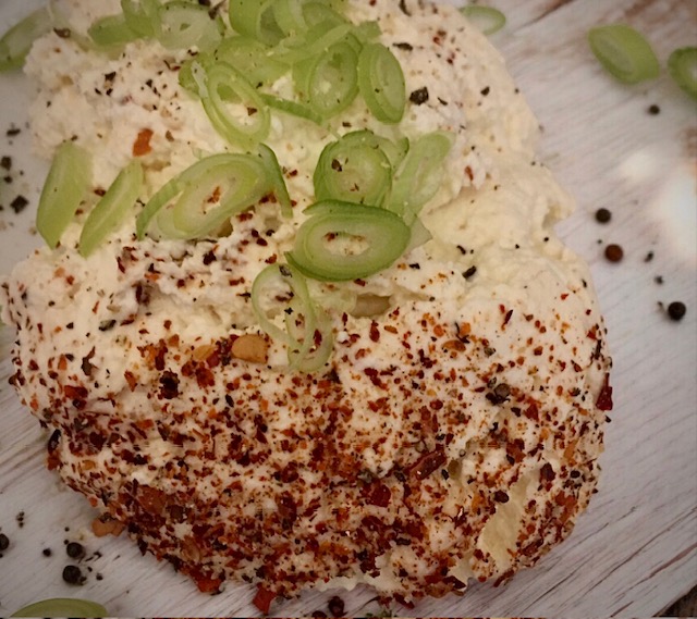 Frischkäse sebst gemacht auf einem Holzbrett mit etwas Chili und Frühlingszwiebeln kleingeschnitten angerichtet.