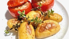 Gefüllte Ofen-Tomaten mit Hackfleisch und kleinen frischen Kartoffeln auf einem weißen Teller serviert und mit Pfeffer dekoriert.