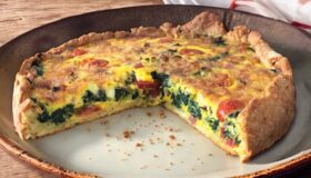 Eine saftige Gemüse Schinken Quiche aufgeschnitten auf einem Teller.
