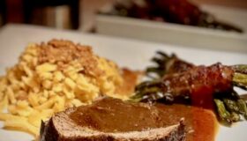 Geschmorte Lammkeule mit Spätzle und gerösteten Semmelbösel mit einer kräftigen dunklen Soße und Bohnen in Speck angerichtet.