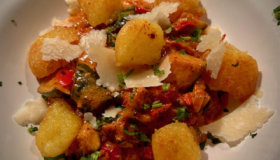 Gnocchi-Gröstl mit würziger Salsiccia und Herbstgemüse auf einem Teller mit Parmesan-Streifen serviert