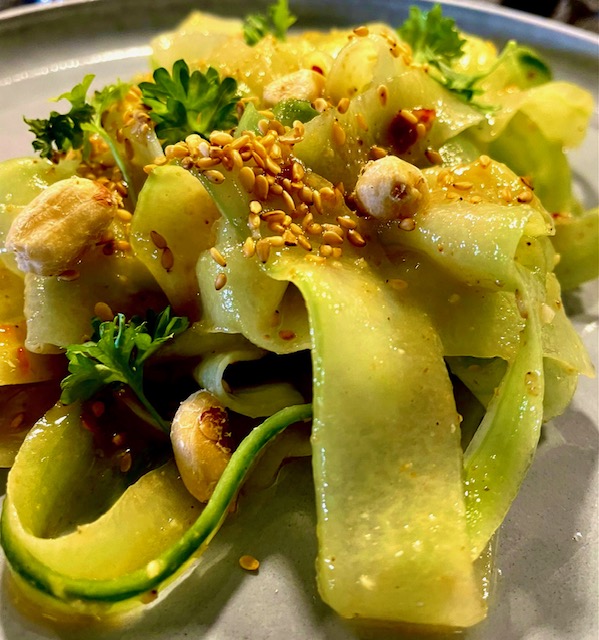 Gurkensalat auf asiatische Art mit gerösteten Sesamsamen und Erdnusskernen auf einem dekorativen Teller angerichtet.