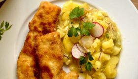 Hähnchenschnitzel mit Kartoffelsalat auf einem weißen Teller serviert.