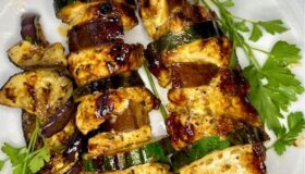 Auf der Teppanyake-Platte gegrillte Hähnchen-/Zucchini-Spieße auf einem weißen Teller angerichtet und mit frischer Petersilie garniert.