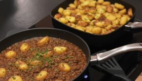 Zwei Pfannen von Pfannen Harecker, gefüllt mit deftigem Hackfleischgericht und knusprigen Bratkartoffeln, bereit für ein köstliches Familienessen.