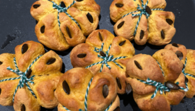 Halloween-Kürbisbrötchen mit grünem Garn auf einer dunklen Schieferplatte.