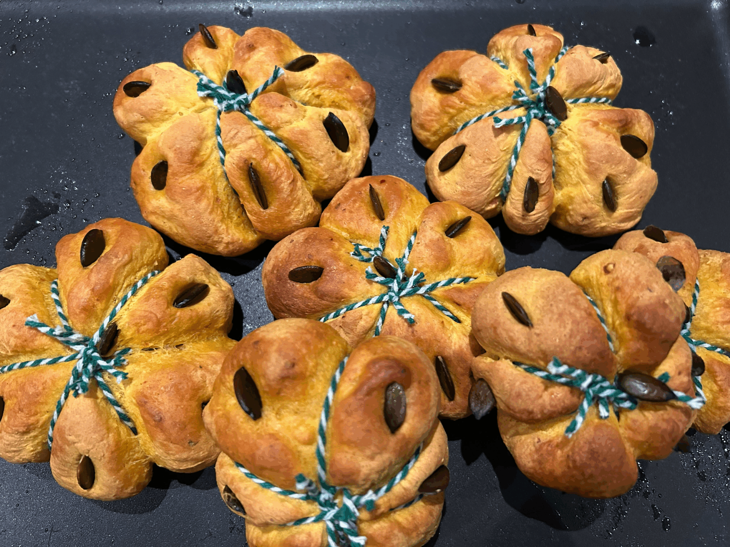 Halloween-Kürbisbrötchen mit grünem Garn auf einer dunklen Schieferplatte.