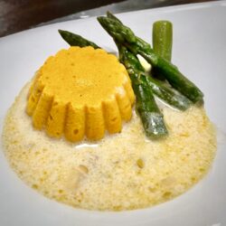 Karottenflan mit grünem Spargel und einer weißen Spargel-Sauce auf einem Teller serviert.