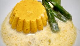 Karottenflan mit grünem Spargel und einer weißen Spargel-Sauce auf einem Teller serviert.