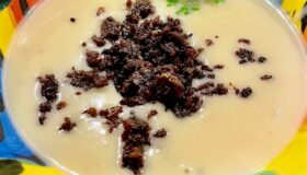 Eine Kartoffel-Kokossuppe mit Pumpernickel-Cruch auf einem bunten Teller angerichtet.