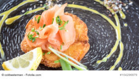 Kartoffelrösti mit Lachs und Limettencrem auf einem dunklen Teller angerichtet.