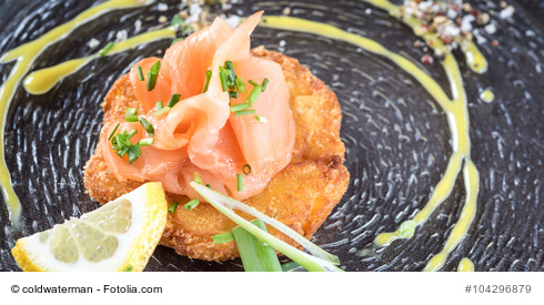 Kartoffelrösti mit Lachs und Limettencrem auf einem dunklen Teller angerichtet.