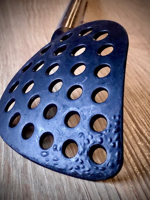 Eine Schaumkelle als Küchenhelfer mit schwarzem Plastik welches Blasen geschlagen hat.