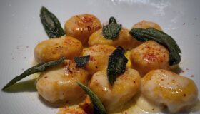 Kürbis-Ricotta-Gnocchi auf einem weißen Teller angerichtet und mit Salbeiblätter dekoriert