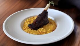 Lammstelze auf Kürbis-Risotto in einem weißen, tiefen Teller angerichtet.
