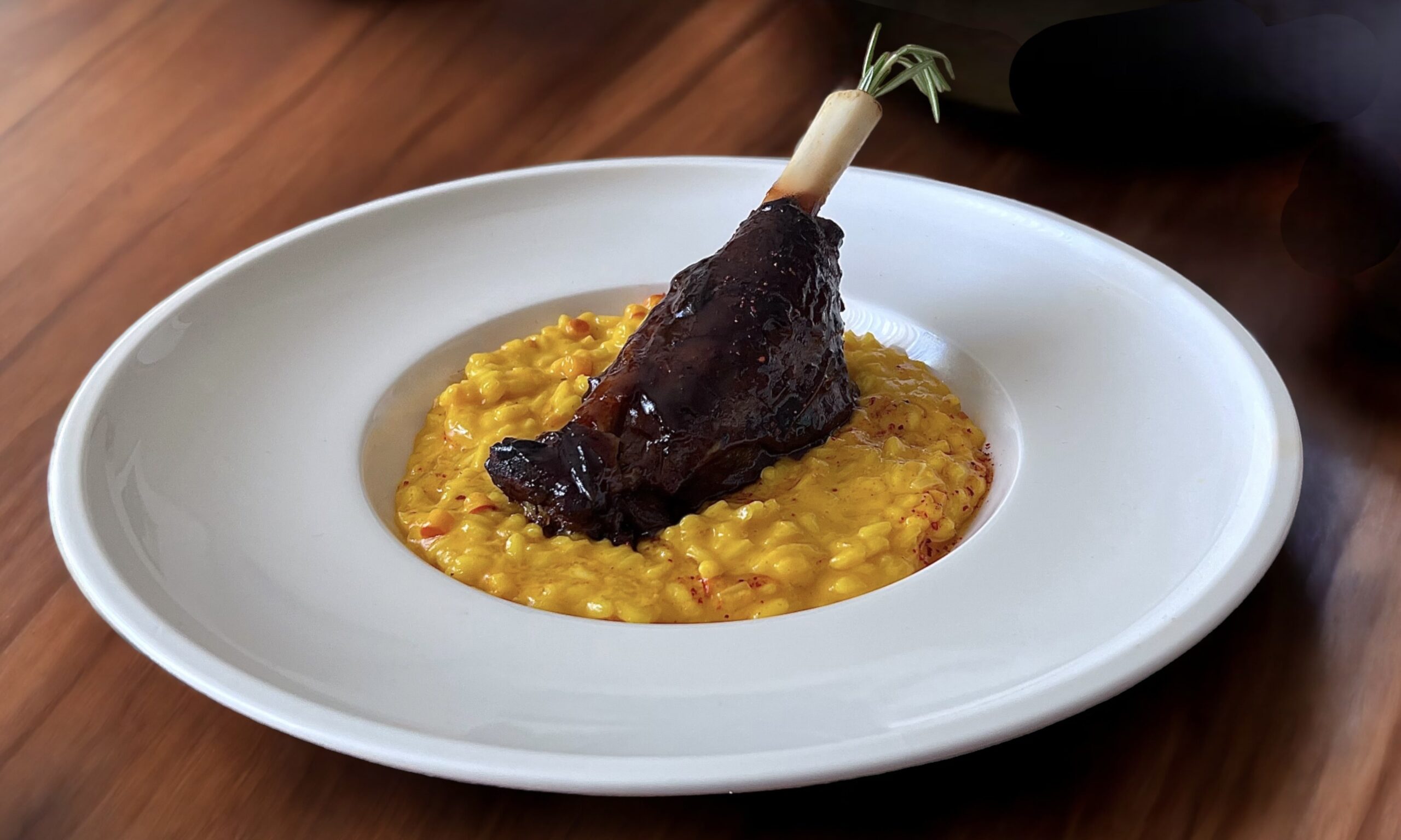 Lammstelze auf Kürbis-Risotto in einem weißen, tiefen Teller angerichtet.