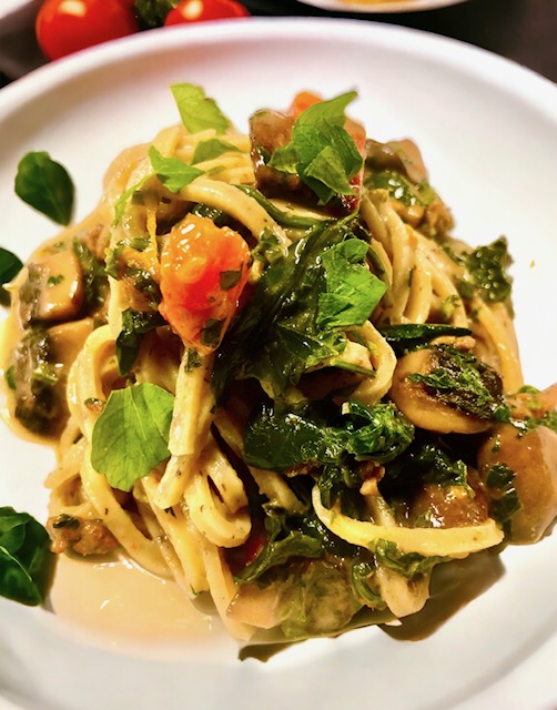 Linguine mit getrüffelten Champignons auf einem hellen Teller serviert und mit frischen Kräutern garniert.