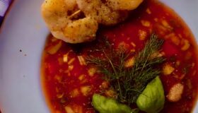 Eine kalte Melonensuppe mit drei knusprigen Garnelen am Spieß auf einem Teller serviert und mit Basilikum garniert.