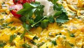Omelett mit Kräutern, darauf ein paar halbierte Tomaten, Petersiele und etwas Sauerrahm.