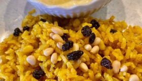 Orientalischer Reissalat mit gerösteten Pinienkernen und Korinthen auf einem dekorativen Teller mit Limetten-Dip serviert.