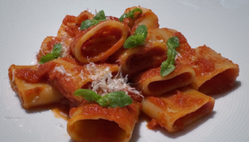 Paccheri - Röhrennudeln mit einfacher Tomatensauce auf einem weißen Teller angerichtet mit Basilikum garniert.