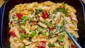 Pasta aus dem Ofen mit Feta, Spinat und Cocktailtomaten in der Auflaufform serviert.