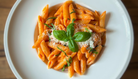 Penne alla Vodka auf einem weißen tiefen Teller serviert und mit etwas Basilikum dekoriert.