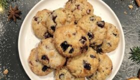 Wenige, festliche Mini-Stollen angerichtet auf einem großen Teller auf einer dunklen Stein-Küchenarbeitsplatte mit weihnachtlicher Dekoration – Inspiration für die Weihnachtsbäckerei mit Pfannen Harecker.