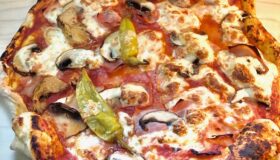 Eine fertige Pizza Regina auf einem Holzbrett.