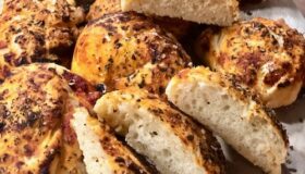 Einige knusprige Pizzabrötchen mit verschiedenen duftenden Kräutern auf einem Brett.