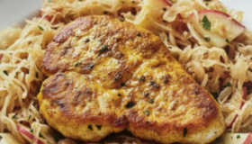 Putenschnitzel gebraten auf einem Apfel-Sauerkraut in einem weißen Teller serviert.