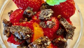 Quarkcreme mit frischen Erdbeeren und karamelisiertem Pumpernickel-Crunch in einer Glasschale serviert.