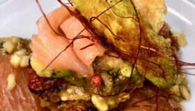 Rösti auf Räucherlachs mit Avocado auf einem weißen Teller serviert.