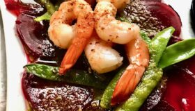 Rote Beete Carpaccio mit Shrimps und Zuckerschoten auf einem weißen Teller serviert.