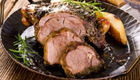 Rustikaler Lammbraten mit feiner Rotwein/Fond-Soße auf einem dunklen Teller angerichtet.