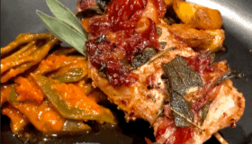 Saltimbocca mit Rosmarinkartoffeln und Bohnengemüse auf einem schwarzen Teller angerichtet.