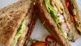Vegetarisches Club-Sandwich halbiert auf einem Teller mit etwas frischem Salat serviert.