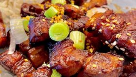 Im Ofen gebackene Schweinebauchwürfel auf einem dekorativen Teller mit Reis und in Ringe geschnittene Frühlingszwiebel garniert.