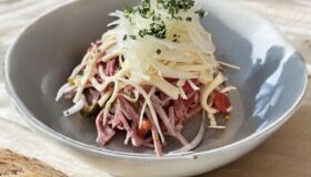 Schweizer Wurstsalat in einer Servierschüssel angerichtet.