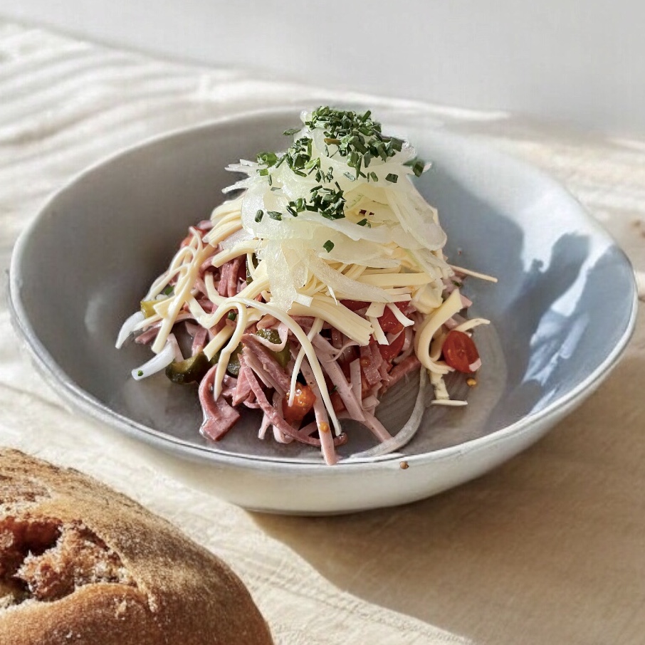 Schweizer Wurstsalat in einer Servierschüssel angerichtet.